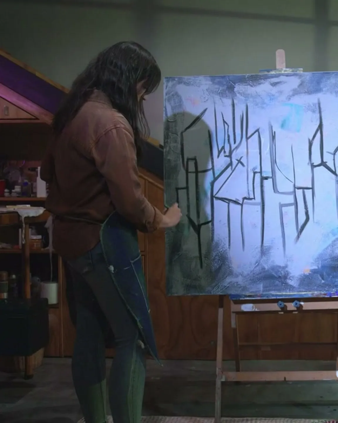 La artista trabajando en su taller, de espaldas frente al lienzo (muestra)